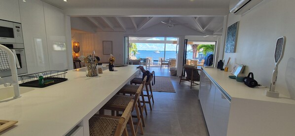A modern kitchen with a long counter, white cabinets, and a view of the sea through large windows. - Waterfront villa 4 bedrooms, 3 bathrooms with pool, kayaks, high speed wifi (Cul-de-Sac)