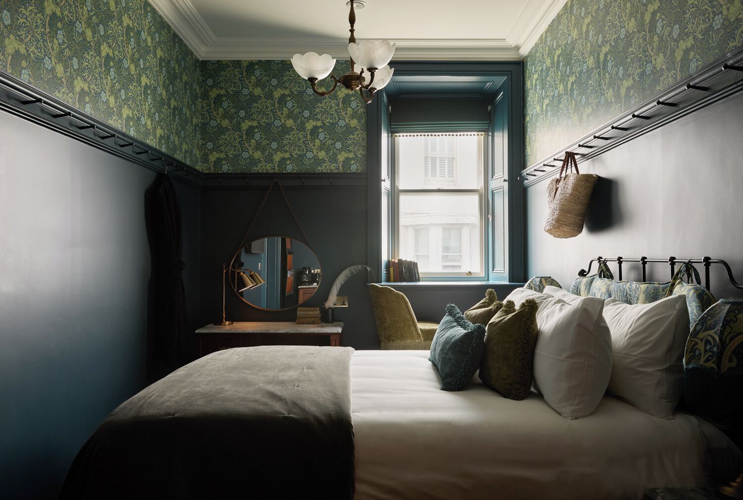 A bedroom with a bed, a mirror, a window, and a hanging basket.