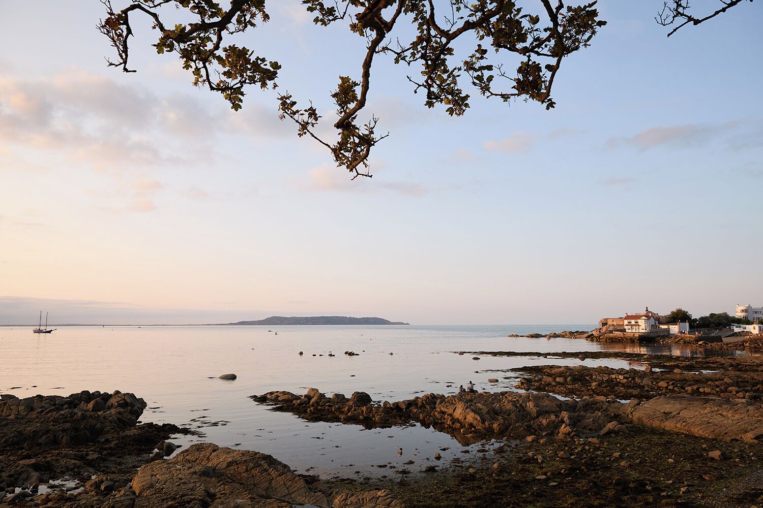 A coastal landscape with rocky shores, calm sea, and distant buildings.