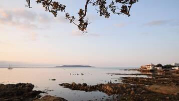 A coastal landscape with rocky shores, calm sea, and distant buildings.