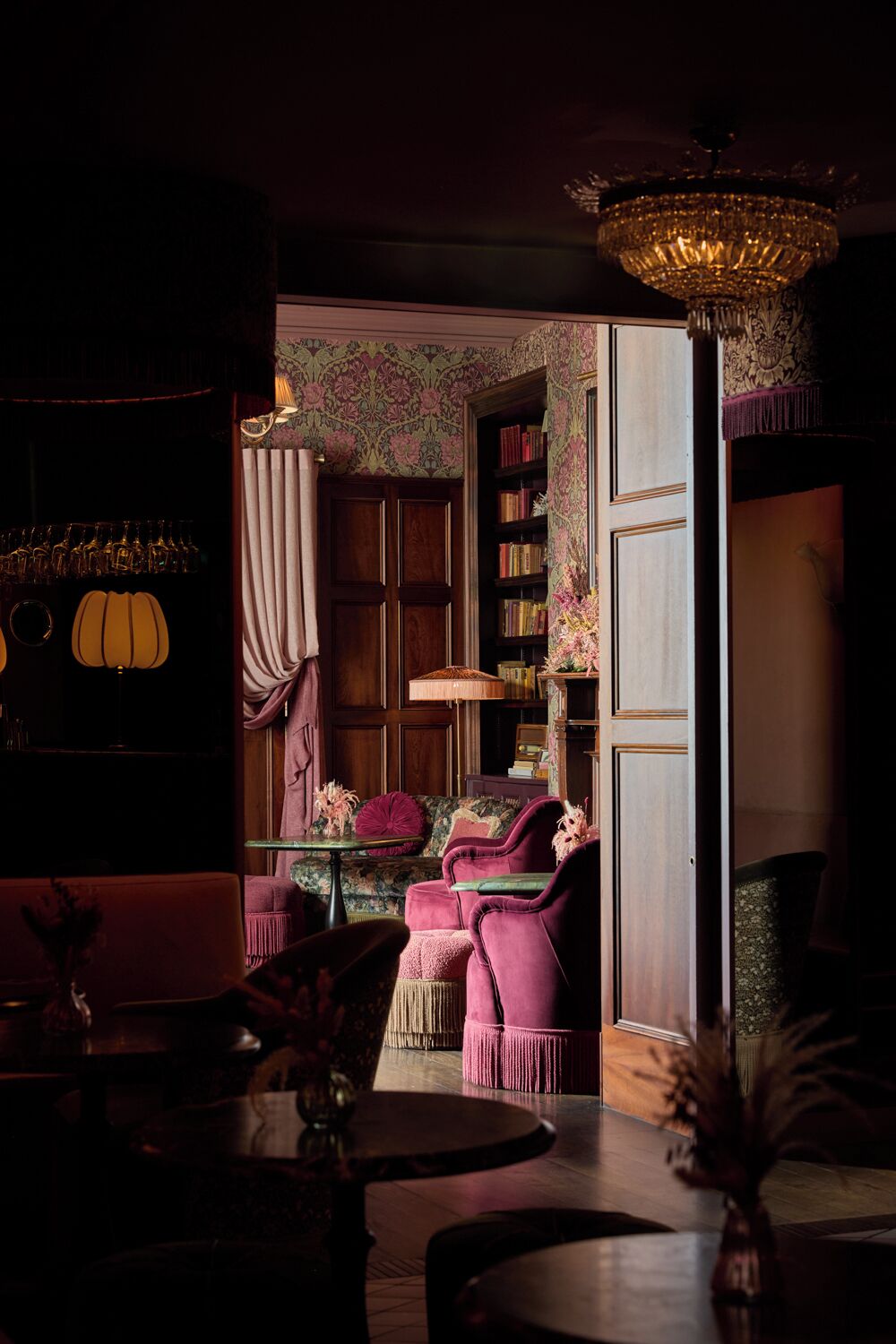A dimly lit room with a chandelier, a bookshelf, and a seating area with a table and chairs.
