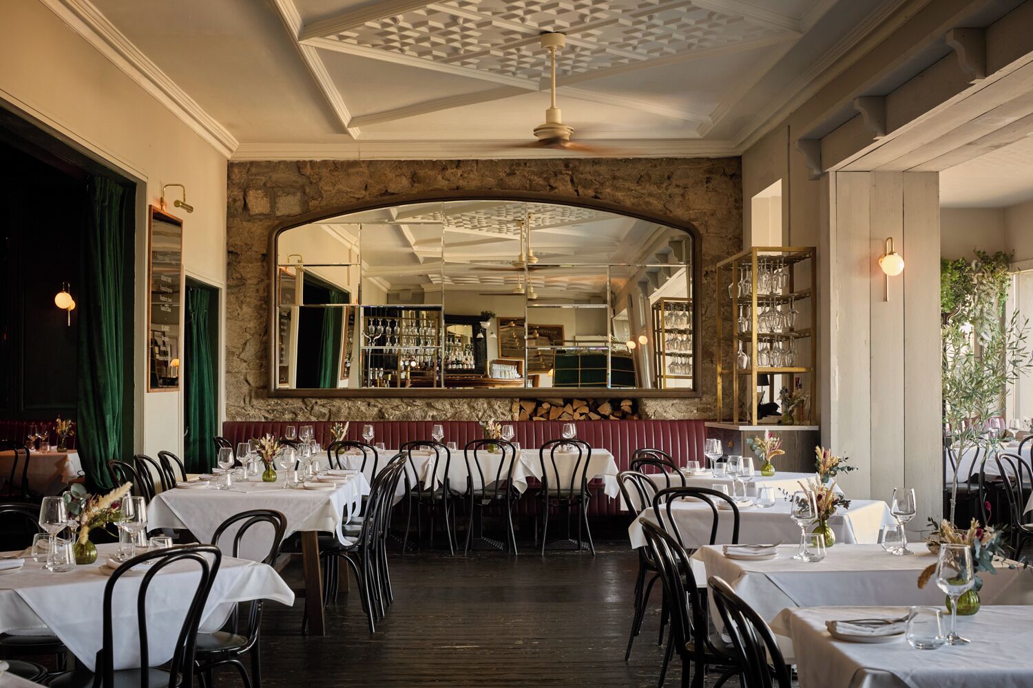 Un restaurante con varias mesas, una pared de piedra y un espejo grande que refleja el interior.