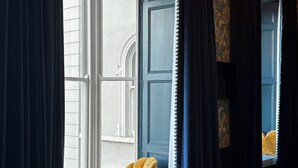 Una habitación de hotel con una cama grande, una ventana con cortinas, una silla y un espejo.
