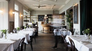 Ein Restaurant mit weißen Tischdecken, Holzbänken und einer Bar.