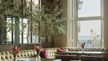 A room with a large window, a sofa, chairs, and a table with vases.