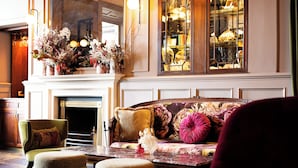 A cozy room with a fireplace, a sofa with floral upholstery, and a large window with a view of the city. - Haddington House Hotel (Dublin)