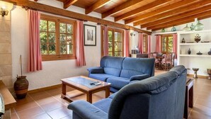 Uma sala de estar ampla com sofá azul, vigas de madeira no teto e um espaço de jantar com mesa e cadeiras.