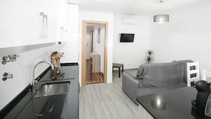 A modern kitchen with a sink, a dining area with a table and chairs, and a grey sofa.
