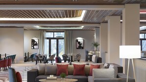 A modern lobby with a sectional sofa, armchairs, a coffee table, and a dining area with chairs and tables. - The Lake Hotel (Ioannina)