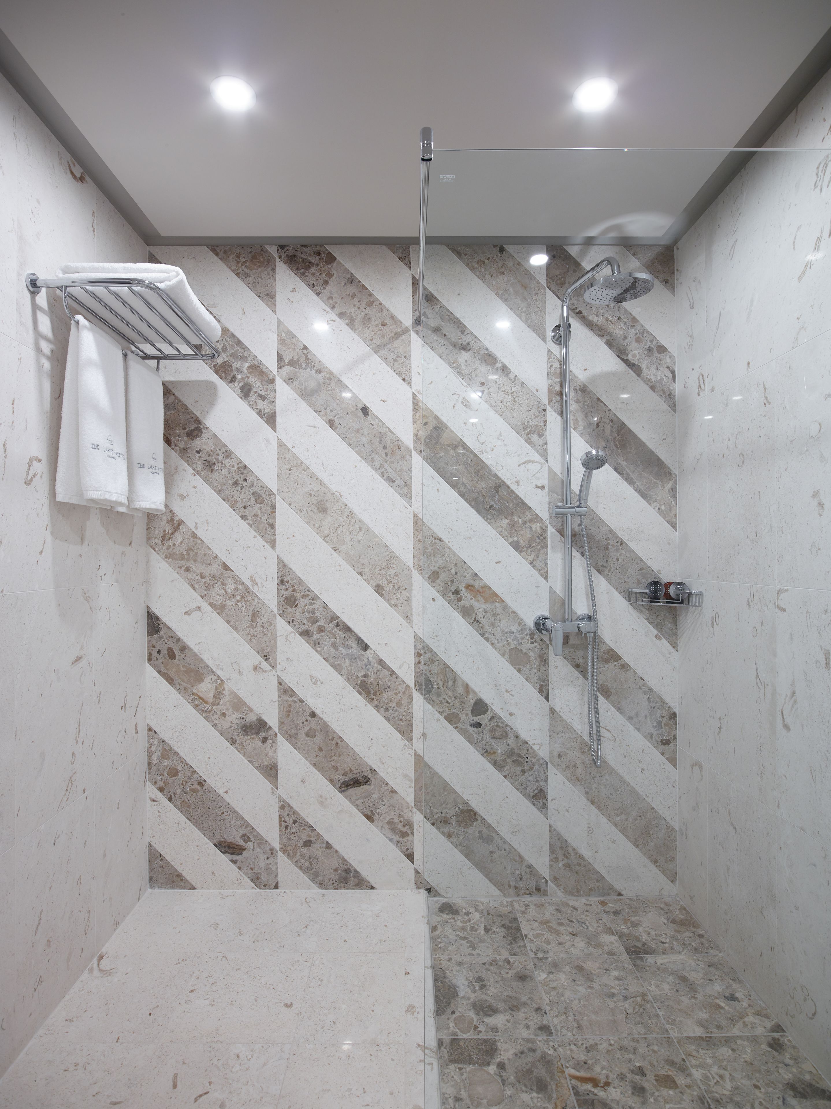 A modern bathroom with a shower, a towel rack, and a marble-patterned wall.