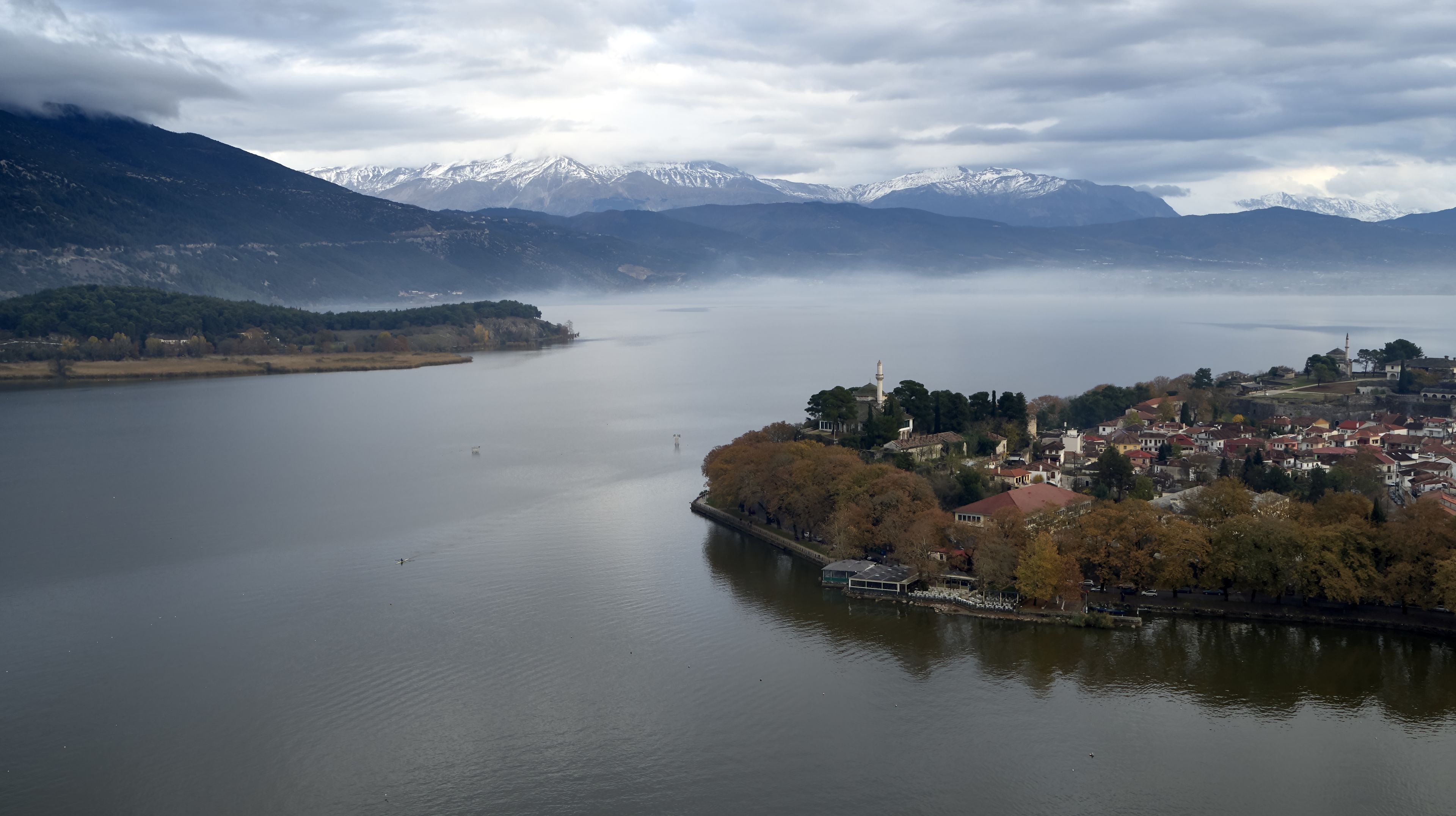 Vista panorámica de un lago con un pueblo a la derecha, destacando una torre imponente y una combinación de edificios residenciales y comerciales.