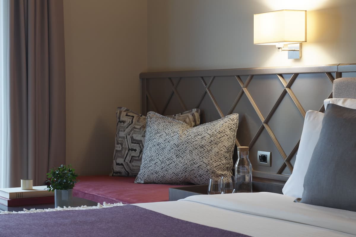 A hotel room with a bed, a nightstand, a lamp, and a wall with a geometric pattern.
