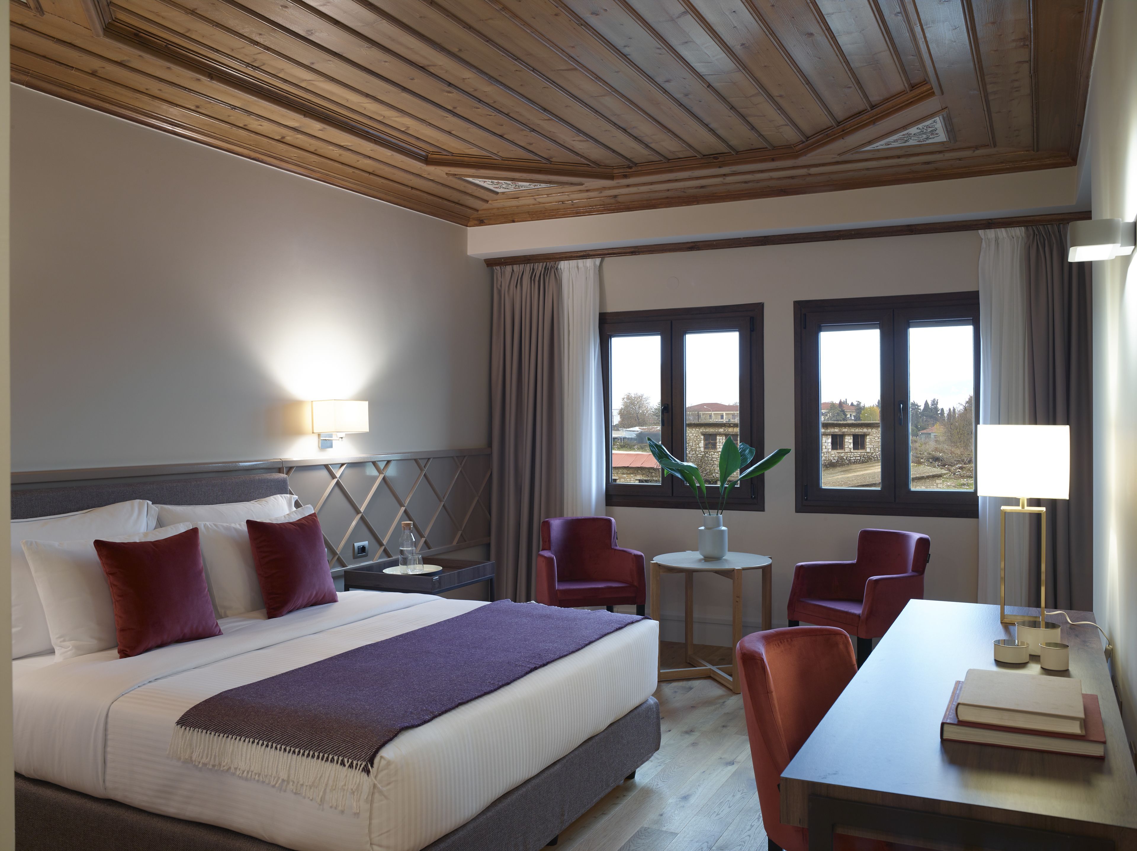 A hotel room with a bed, two chairs, a small table, and a view of the outside.