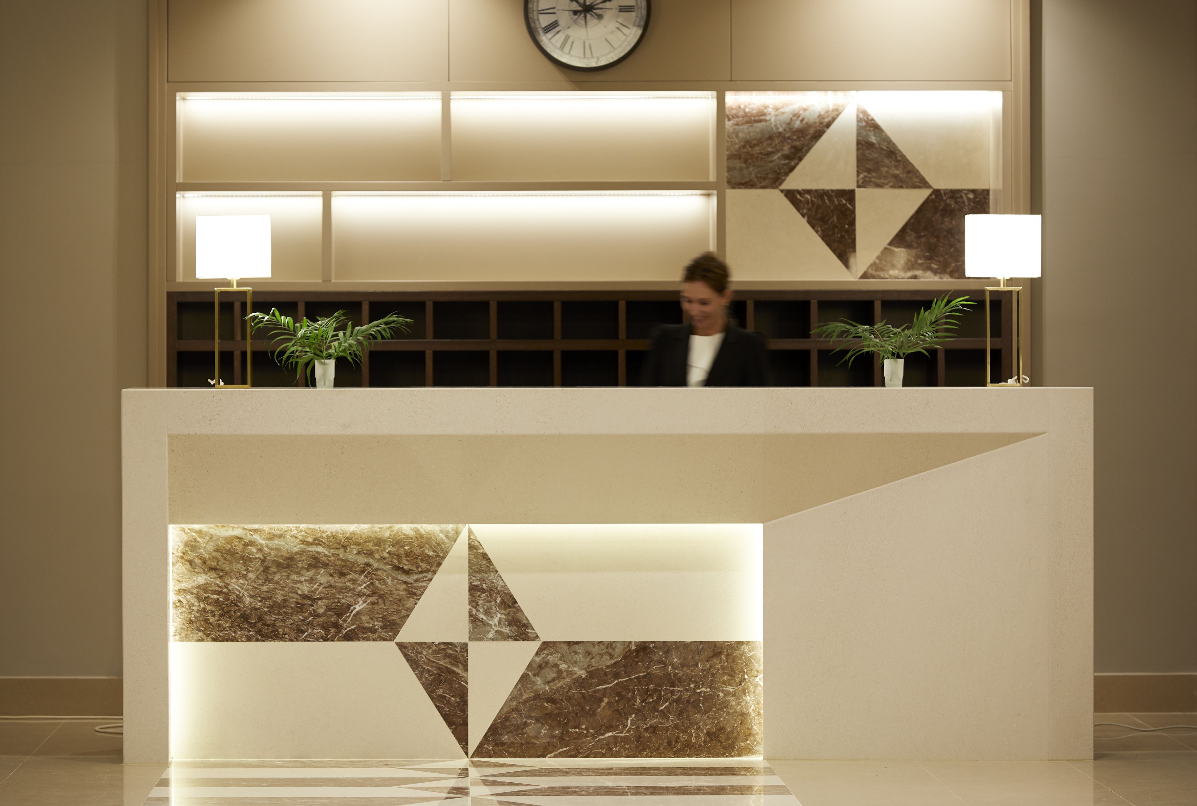 A reception desk with a geometric marble design, a clock, and two potted plants.