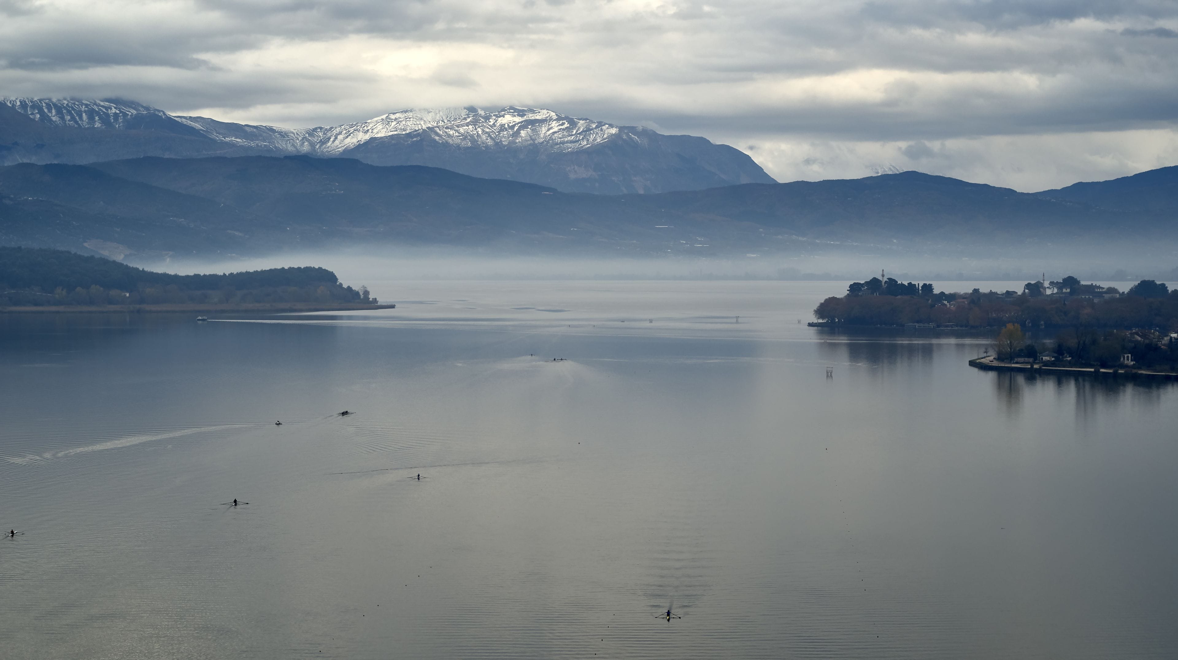 Un lago tranquilo con montañas al fondo y una pequeña isla con edificios.