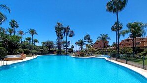 Una gran piscina al aire libre rodeada de palmeras y un edificio al fondo.