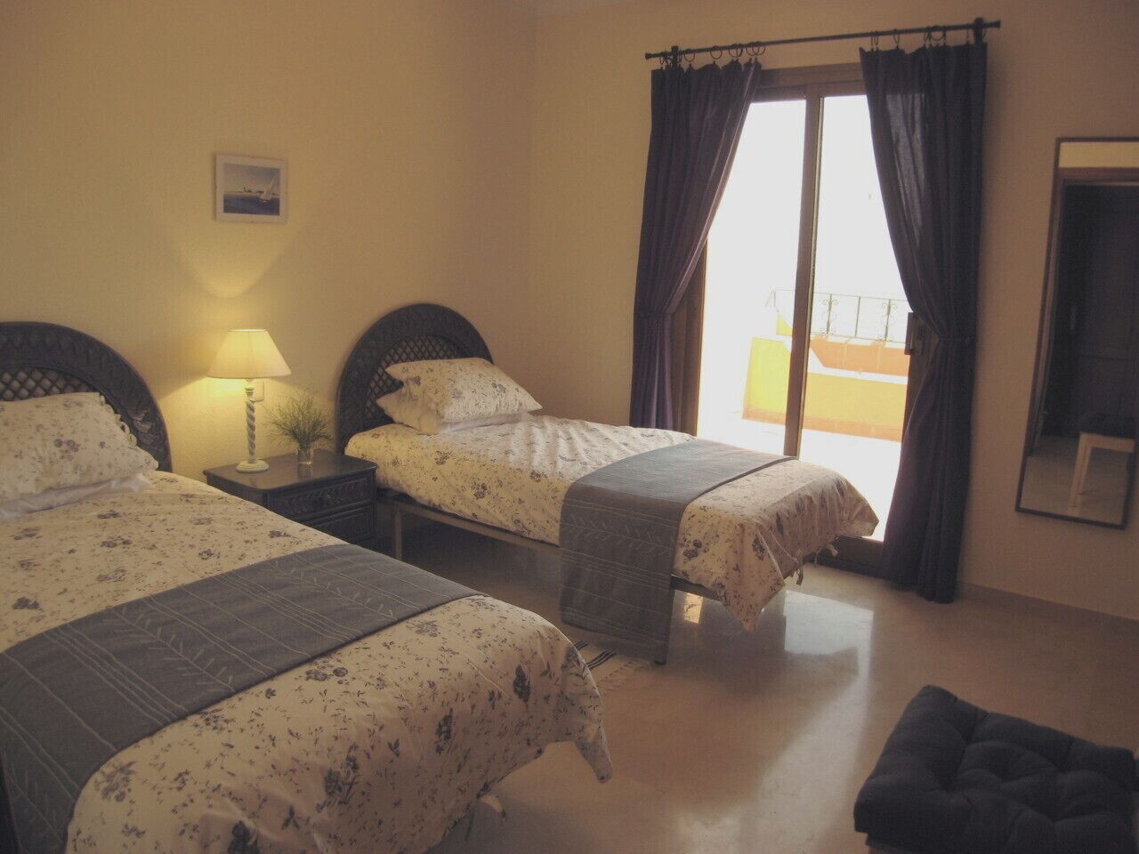 Habitació d'hotel amb dos llits, una taula de nit amb una làmpada, una finestra amb cortines i una petita banca.