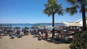 Una playa con tumbonas, sombrillas y palmeras.