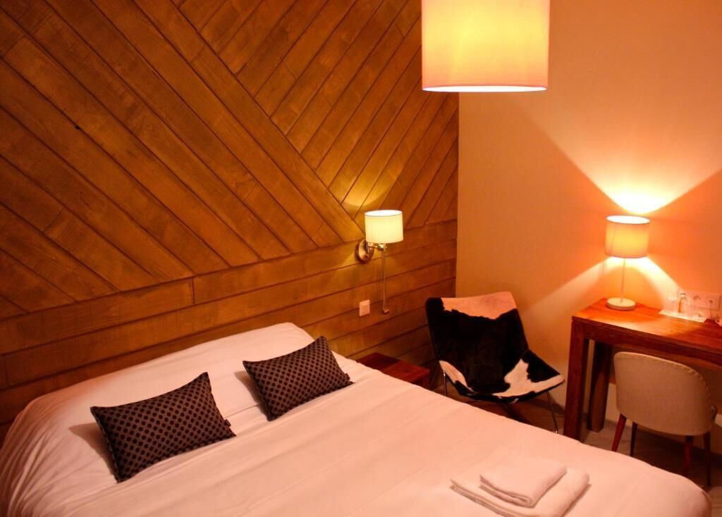 Ein Hotelzimmer mit Holzboden, einem Bett mit zwei Kissen, einem Schreibtisch mit Lampe und einem Sessel.