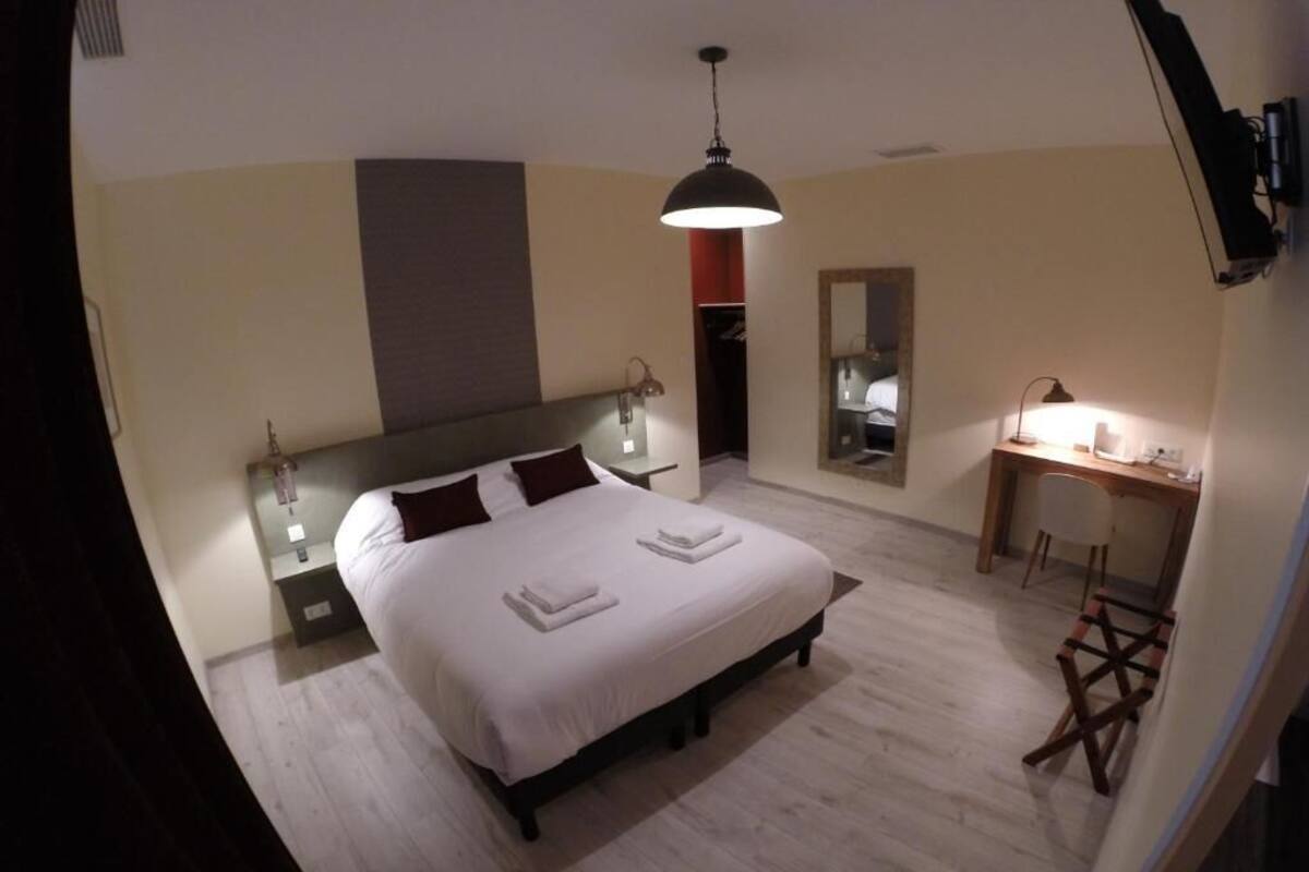 A bedroom with a bed, bedside lamps, a desk, and a mirror.