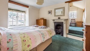 Ein Schlafzimmer mit Bett, Kamin, Fenster und einer Treppe, die zu einer oberen Etage führt.