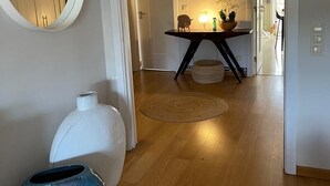 Un couloir doté d’un plancher en bois, d’un miroir rond, d’un vase blanc et d’une table ornée d’objets décoratifs.