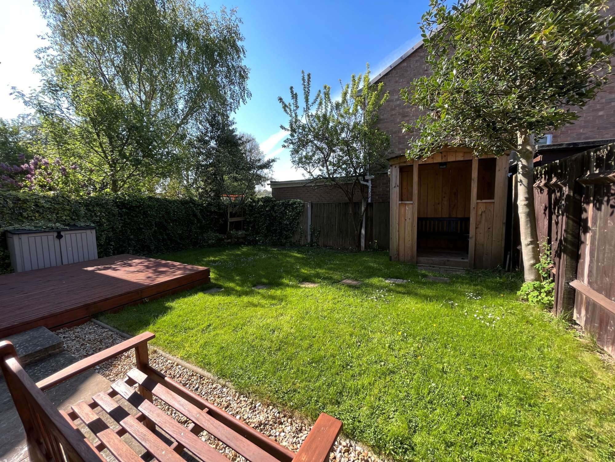 A backyard with a wooden deck, a grassy lawn, and a wooden fence.