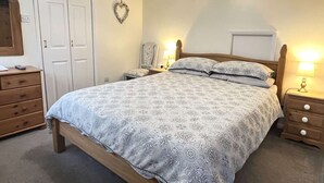 A bedroom with a bed, bedside tables, a dresser, a mirror, and a heart-shaped decoration on the wall.