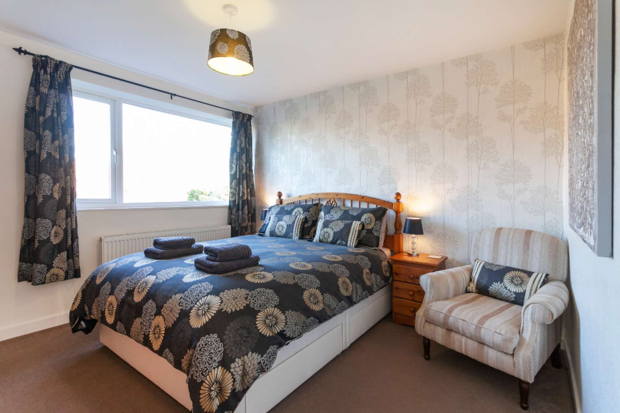 A bedroom with a bed, a chair, a nightstand, a lamp, and a window.