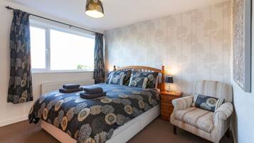 A bedroom with a bed, a chair, a nightstand, a lamp, and a window.