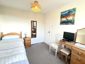 A bedroom with a bed, bedside table, lamp, chair, desk with a TV, and a painting on the wall. - Lovely 4 bedroom detached house in Southwell (Southwell)