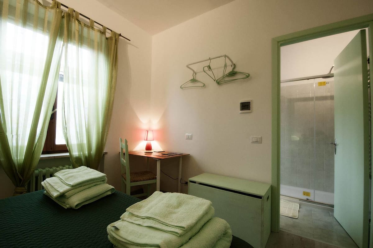 Une pièce comprenant un lit, un bureau avec une lampe, une chaise, un radiateur, une petite table et un espace douche.