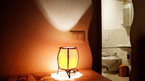 A room with a table lamp, a small table, and a view of a bathroom with a sink and toilet. - B&B La Rosa di Orvieto (Orvieto)