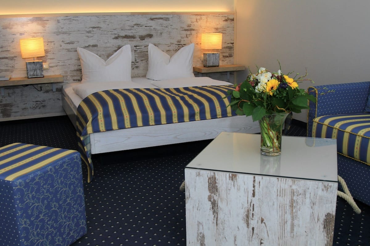 Una habitación de hotel con una cama, dos mesitas de noche con lámparas, un jarrón con flores, un sofá y una mesa de centro.