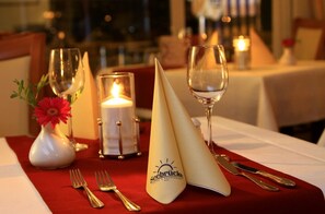 A dining table set with a white napkin, a glass, a candle, a vase with a red flower, and a fork. - Hotel Seebrücke (Zingst)