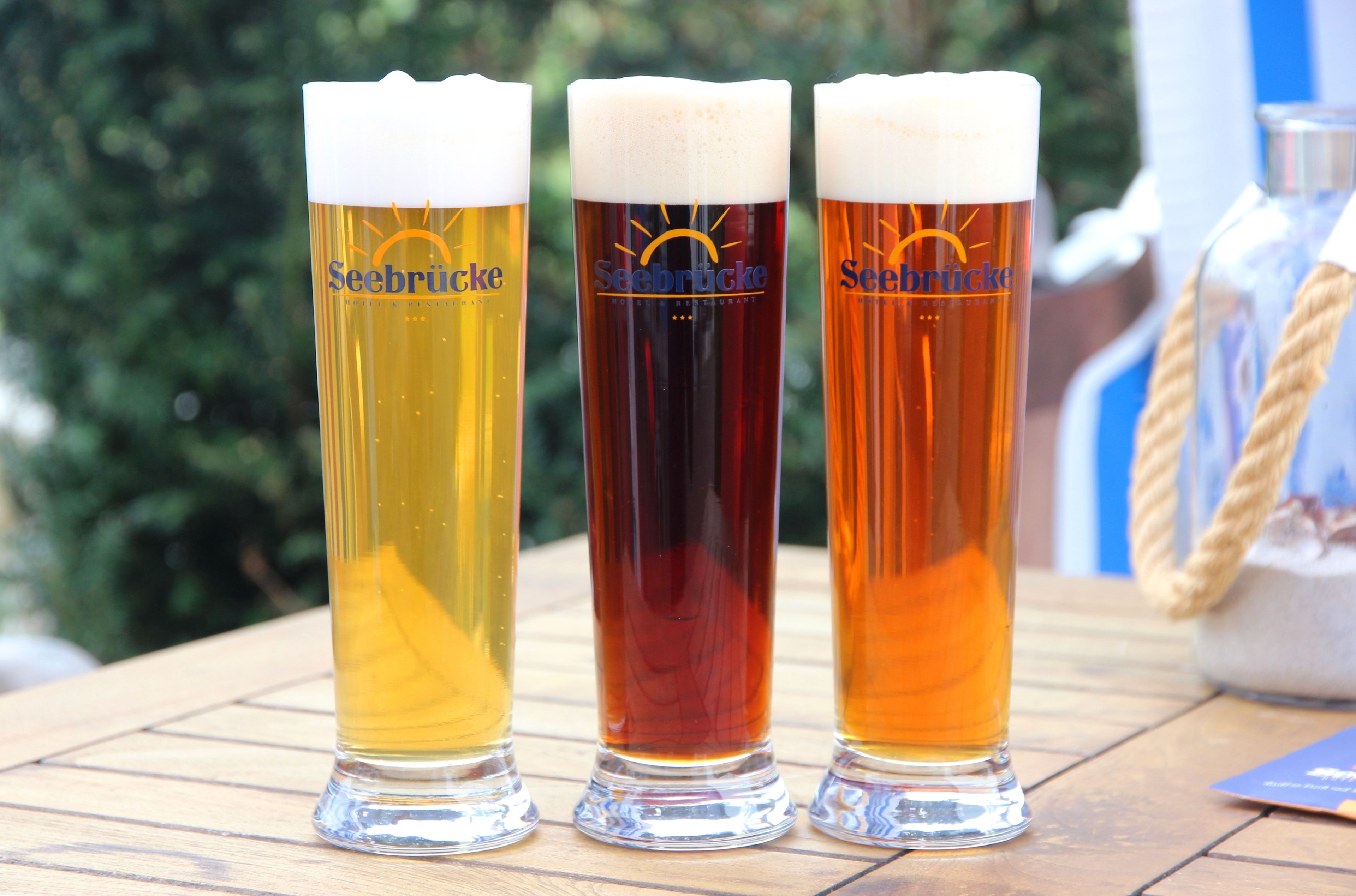 Three Seebrucke beer glasses on a wooden table with a rope and a bag in the background.