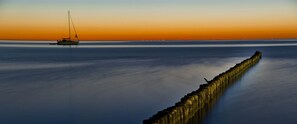 A calm sea at sunset with a sailboat and a long pier extending into the water. - Hotel Seebrücke (Zingst)
