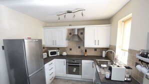 Una cocina compacta con gabinetes blancos, electrodomésticos de acero inoxidable y salpicadero de azulejos.