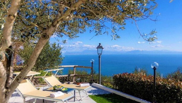 Eine Terrasse mit Lounge-Möbeln, einem Tisch mit Pflanze und Blick auf das Meer.