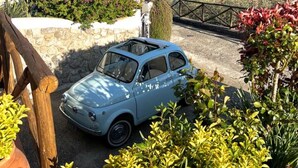Ein hellblaues Auto steht auf einem gepflasterten Platz mit Blick auf das Meer.