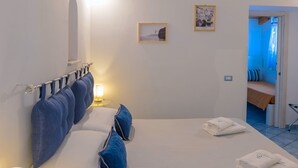 Ein Hotelzimmer mit einem großen Bett, einem Nachttisch mit einer Lampe, einer Wand-Klimaanlage und einer Tür zu einem anderen Raum.