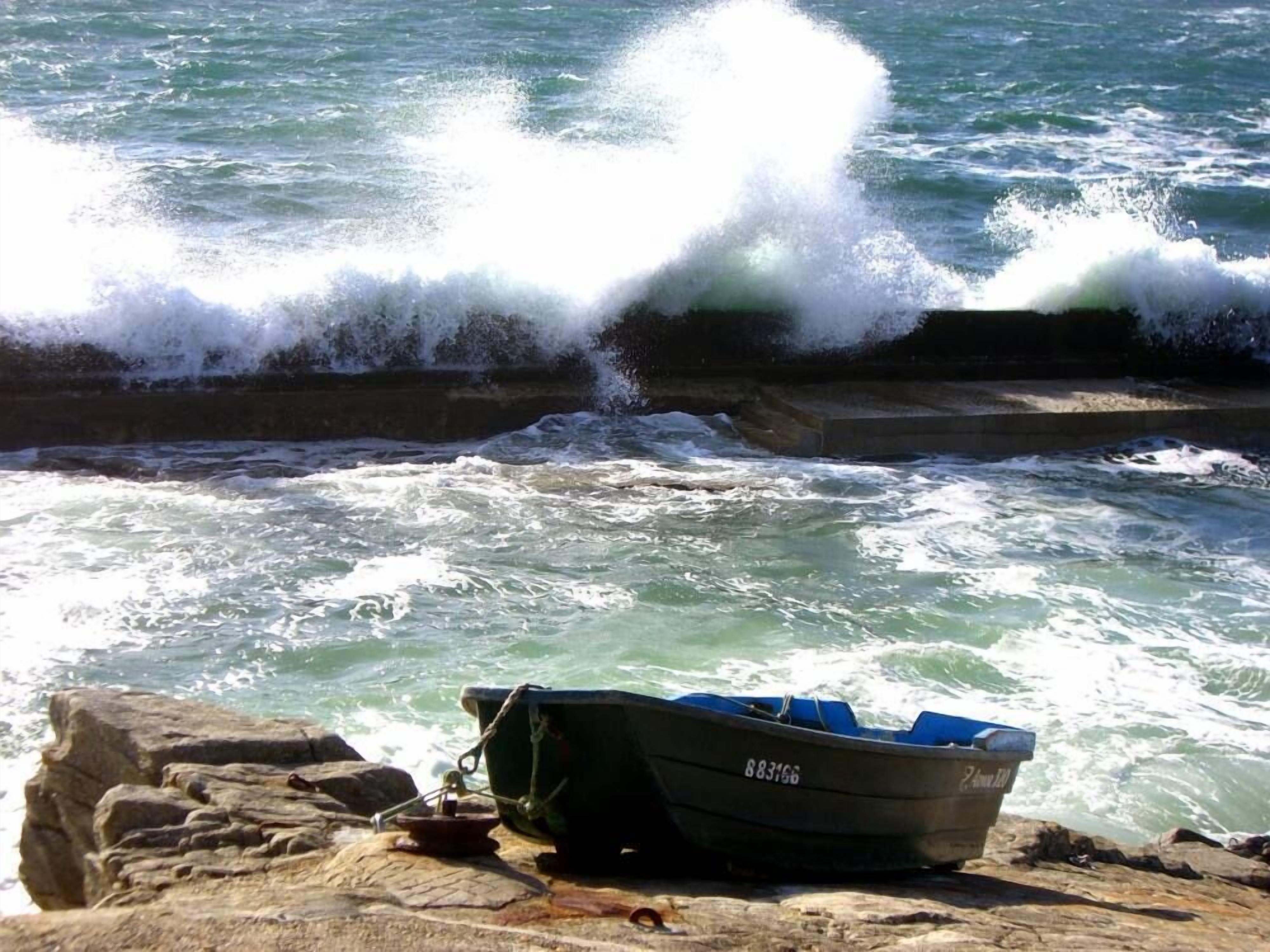 A boat tied to a rocky shore with waves crashing against a concrete barrier.