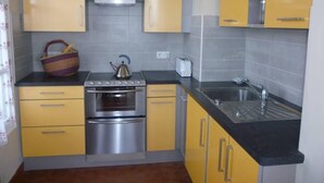 Une cuisine de taille réduite avec des meubles de couleur jaune, une cuisinière en acier inoxydable et un évier.
