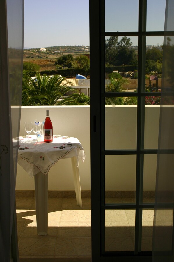 A balcony with a table set for two, a bottle of red wine, and a view of a rural landscape.
