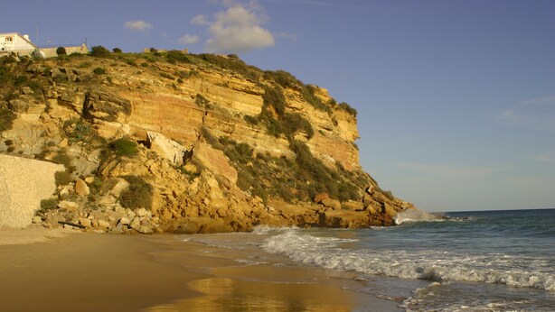 A coastal landscape with a rocky cliff and a sandy beach.