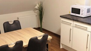Uma sala de jantar com uma mesa e cadeiras de madeira, um micro-ondas branco numa bancada e um radiador ao fundo.
