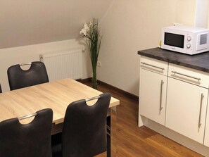 Een eetgedeelte met een houten tafel en stoelen, een witte magnetron op een aanrecht, en een radiator op de achtergrond.