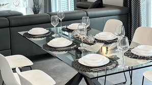 Un comedor moderno con una mesa de vidrio preparada para seis personas, rodeada de sillas blancas.