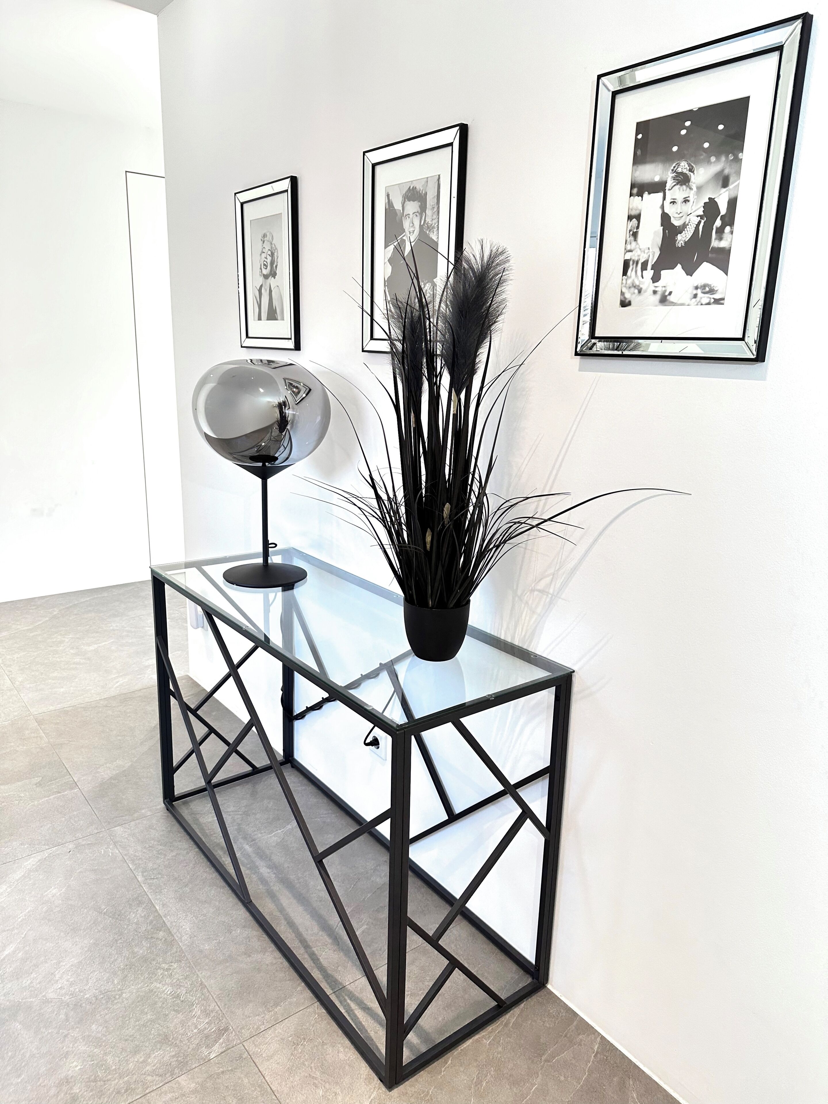 A modern interior with a glass-top console table, a black floor lamp, and three framed pictures on the wall.