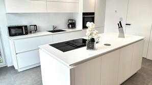 Una cocina moderna con armarios blancos, microondas integrado, cafetera y un lavabo.